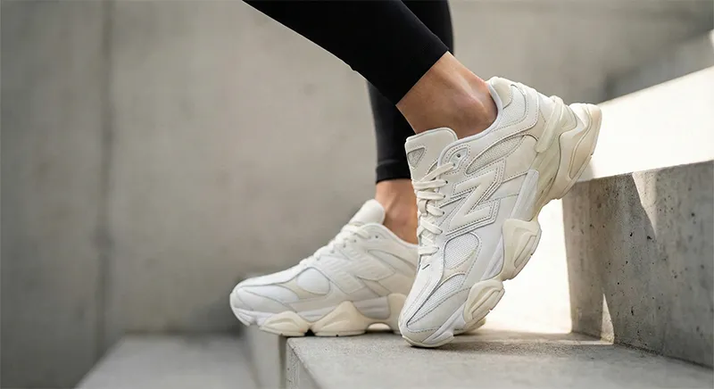 볼륨감 있는 흰색 뉴발란스 9060 운동화를 신은 여성의 발목이 날씬해 보이는 착용샷. 콘크리트 계단 위에서 찍은 로우 앵글 사진이다.