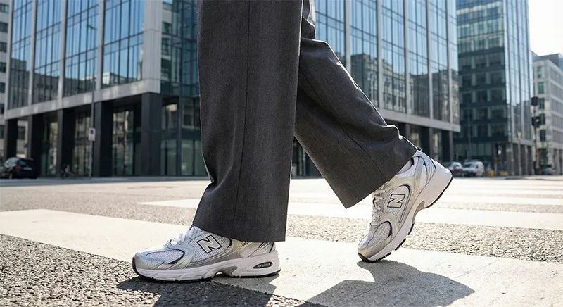 도심 횡단보도에서 차콜색 와이드 슬랙스에 뉴발란스 530 스틸 그레이 운동화를 신고 걷는 모습을 포착한 로우 앵글 사진.