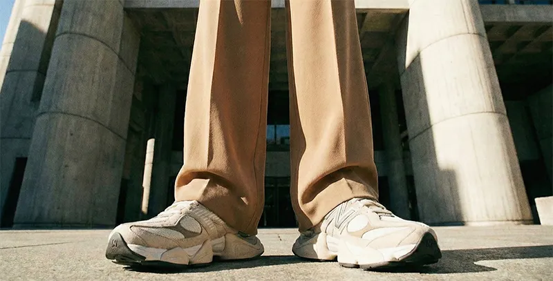 웅장한 콘크리트 건물 앞 로우 앵글 사진. 베이지색 와이드 팬츠 아래로 볼륨감 있는 뉴발란스 9060 운동화가 돋보인다.